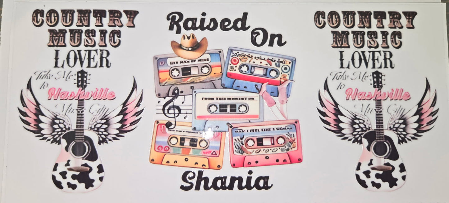 A personalized country music themed banner or print featuring the text 'COUNTRY MUSIC LOVER', 'Raised On', and 'Shania', with illustrated cassette tapes, a guitar, wings, and cow-print details on a white background.